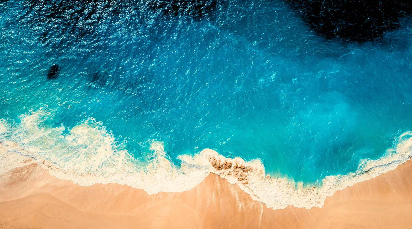 Alt text: "Aerial view of a serene beach where turquoise waves gently meet the golden sands, depicting the tranquil interface of sea and shore