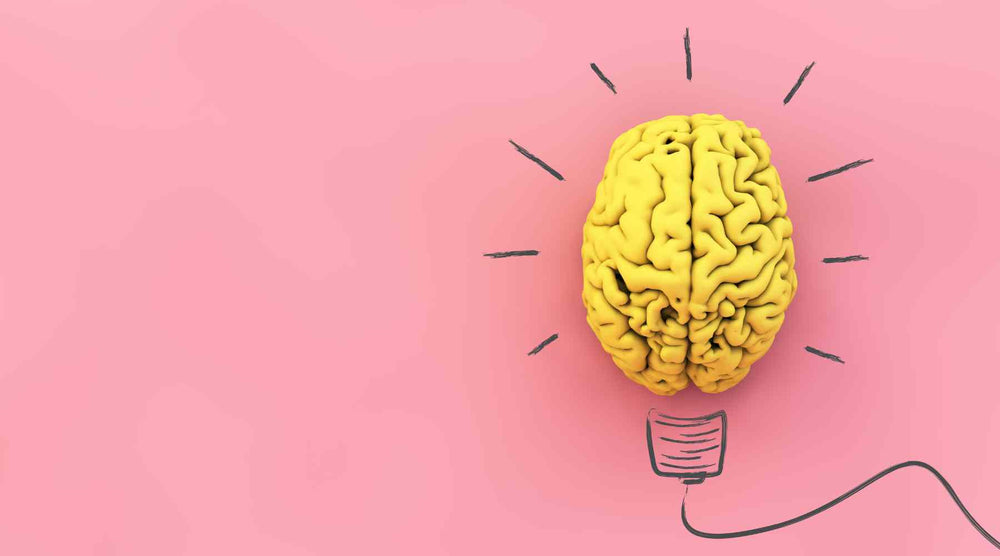The image shows a creative and conceptual design where a human brain is stylized as a lightbulb on a pink background. The brain is yellow, with its grooves and folds highly detailed, and it is positioned at the center of the image. Around the brain, there