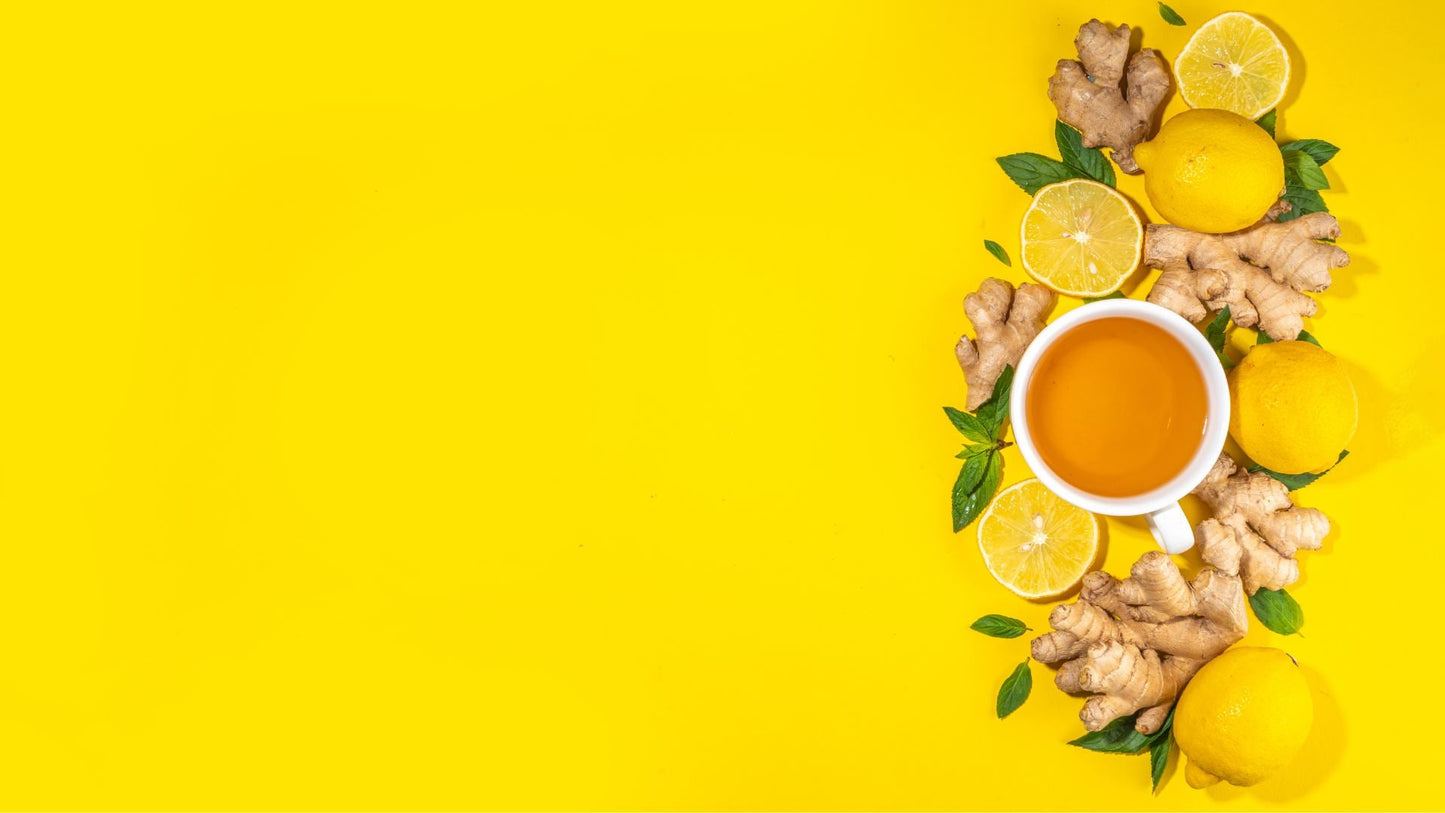 The image shows a cup of ginger, lemon, and honey tea surrounded by fresh ginger roots, lemons, and mint leaves on a yellow background.