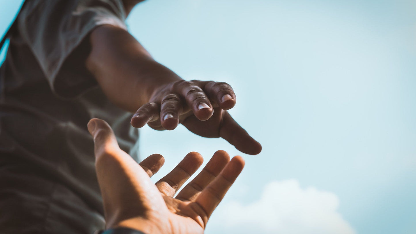 An image captures a moment of humanity — one hand reaching out towards another against a clear sky, symbolizing support, trust, and the essence of good deeds as one person offers help to another.